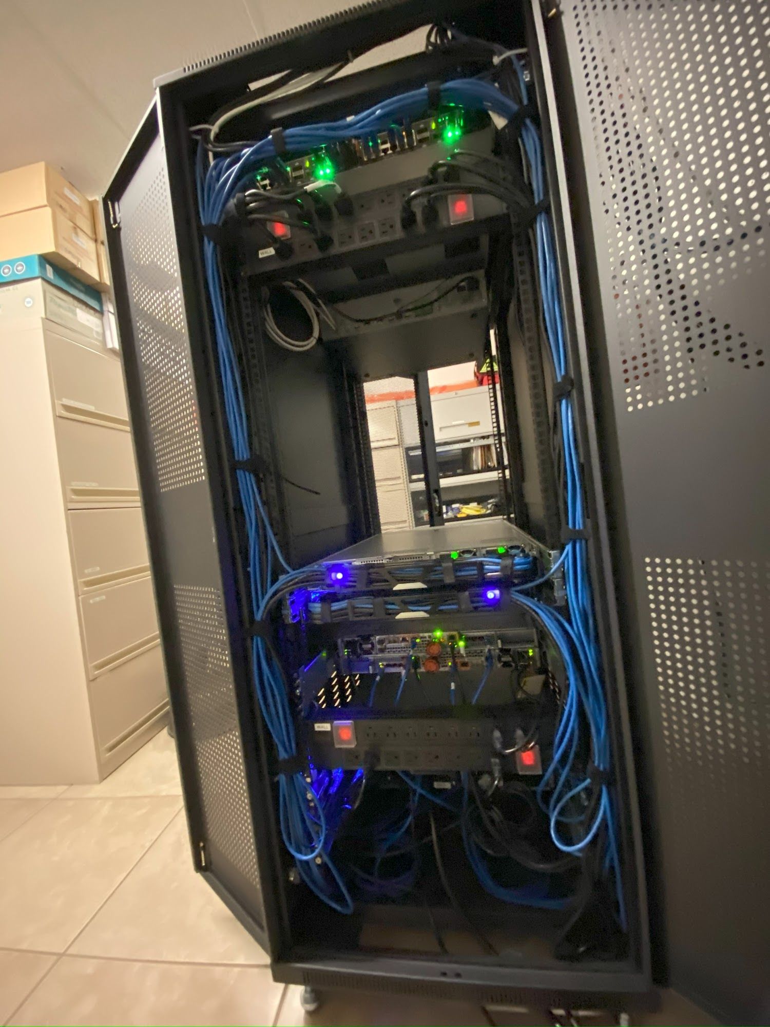A server rack with blue cables, containing various network devices and power supplies, in a room.