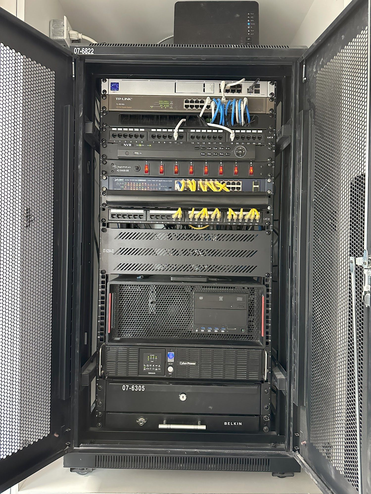 Black server rack cabinet with equipment inside, doors open, indoors.