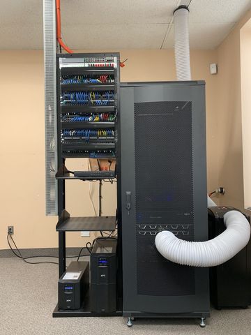Server racks with networking equipment and cooling vent in a room.