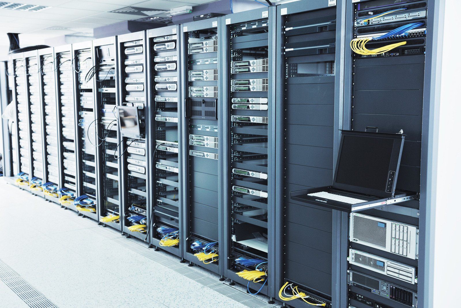 Server racks lined up in a data center, with cables and a laptop.