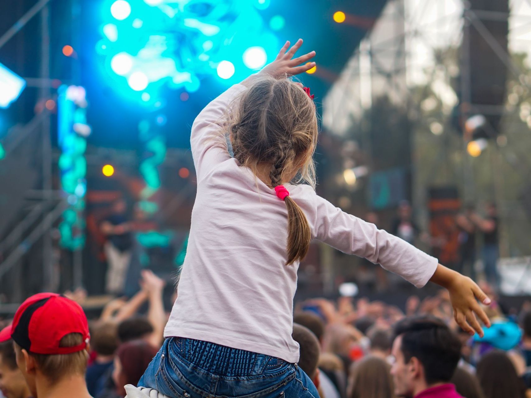A little girl is sitting on a man 's shoulders at a concert.