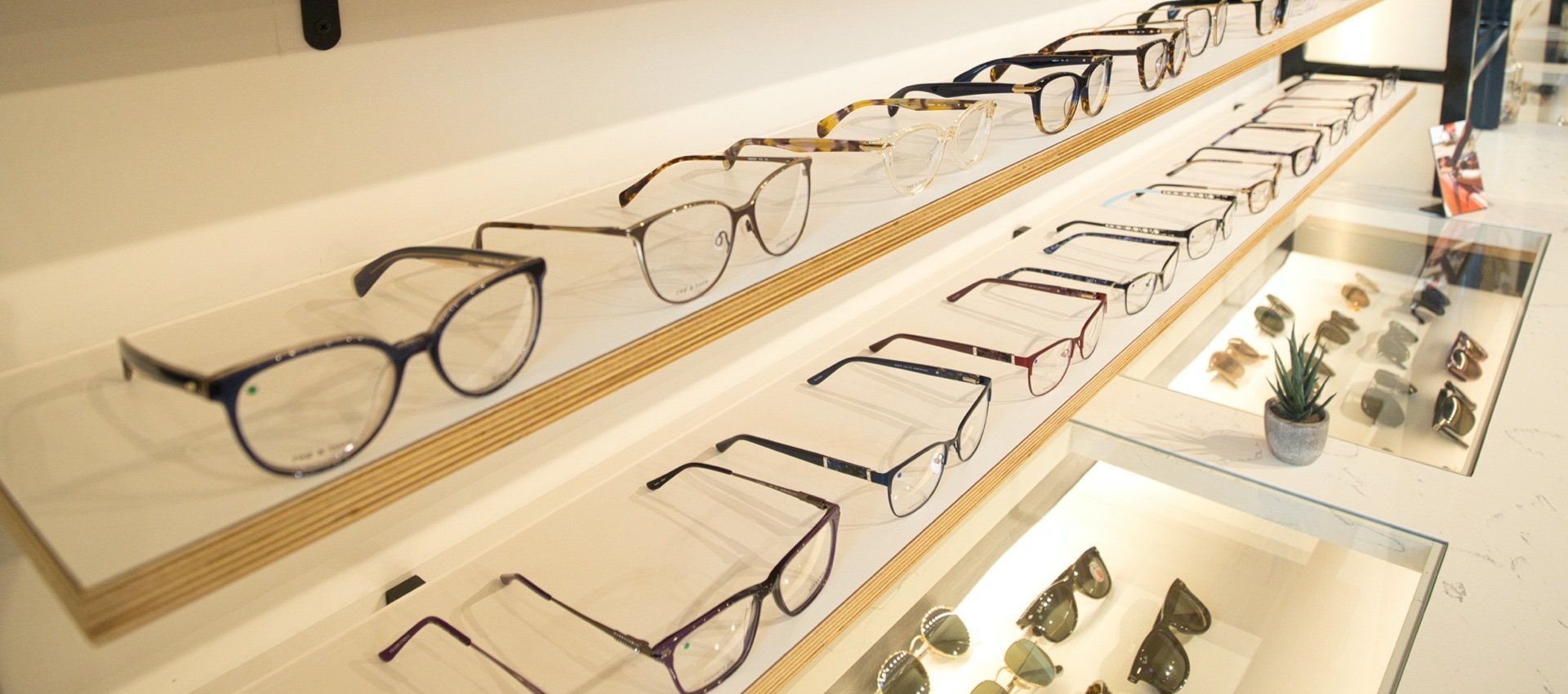 Eyeglasses displayed on shelves in a store, with some sunglasses visible below.