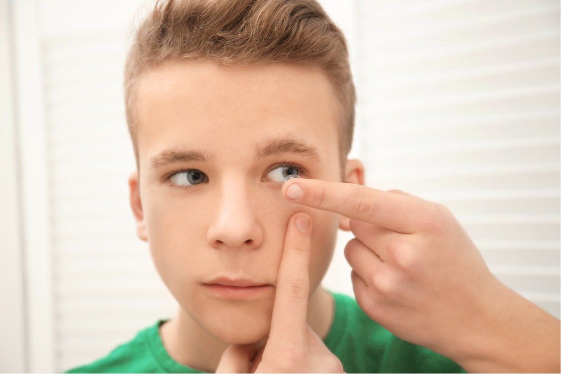 Adolescent male putting contact lens in left eye
