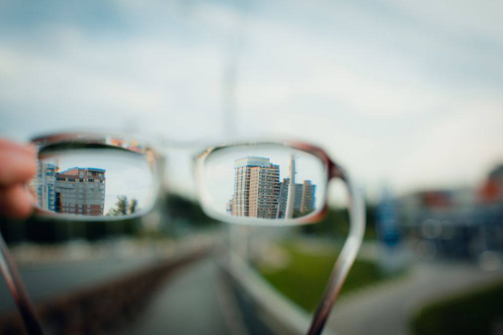 A person is holding a pair of glasses with a reflection of a city in the lenses.