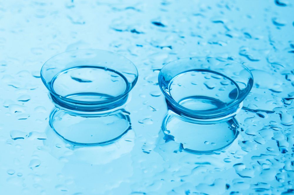 Two contact lenses are sitting on a blue surface with water drops.