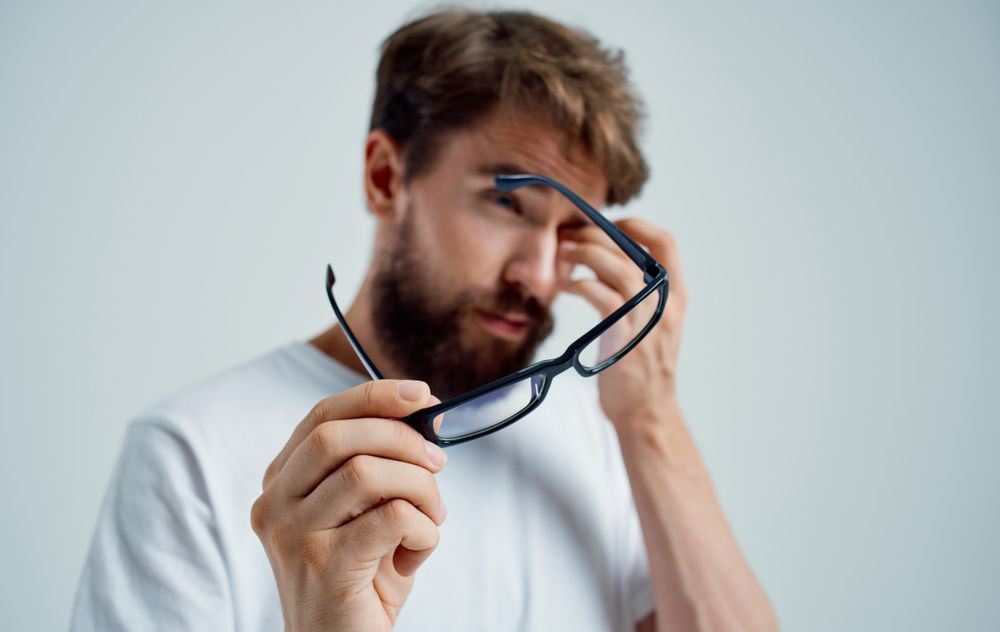 Man holding glasses, rubbing eye, looking tired.