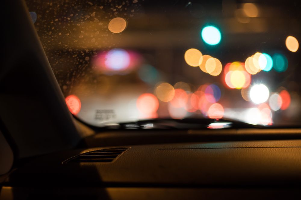 Interior car view at night, looking out at blurry city lights; dashboard in focus.