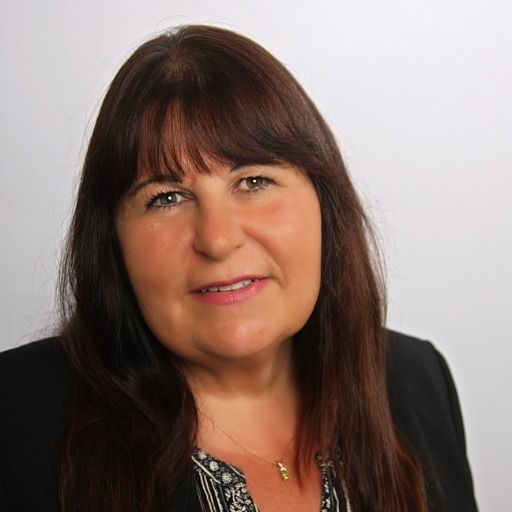 A woman with long brown hair and a necklace is smiling for the camera.