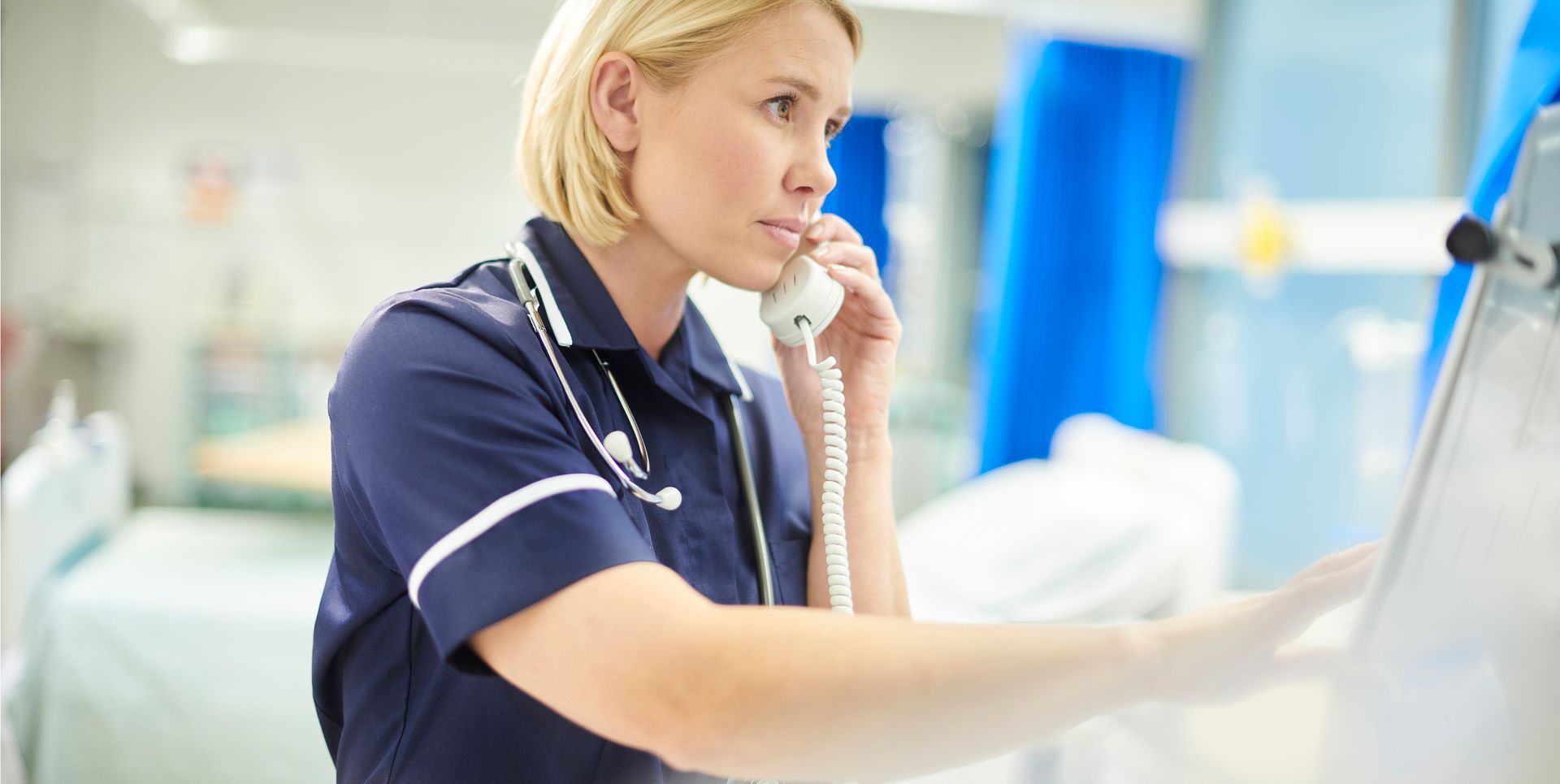 A nurse is talking on a phone in a hospital room.