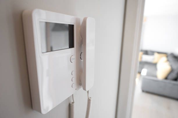 A white video door phone is hanging on a white wall.