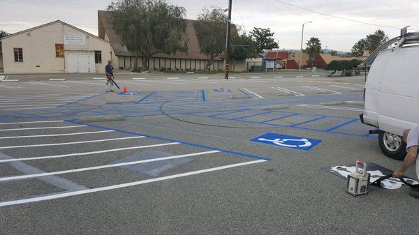 A man is painting a handicapped parking spot in a parking lot.