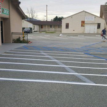 A man is walking down a parking lot in front of a building.