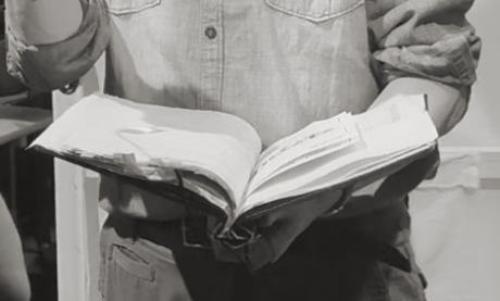 Person, von der man den Kopf nicht sieht, hält aufgeschlagenes Buch, schwarzweiss