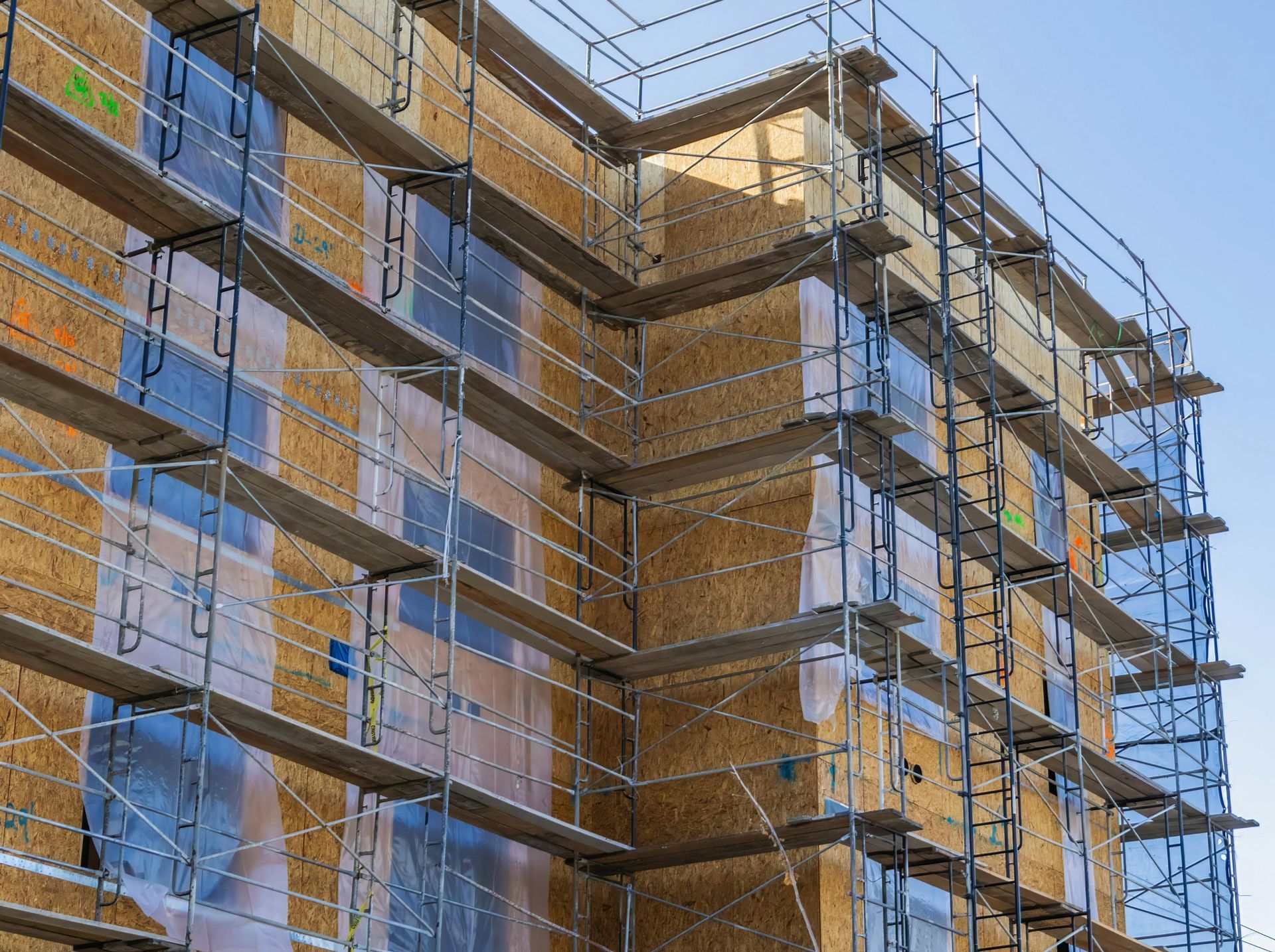 Building under construction surrounded by blue scaffolding and safety netting