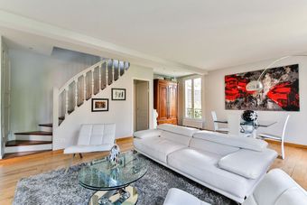A living room with a white couch , chairs , coffee table and stairs.