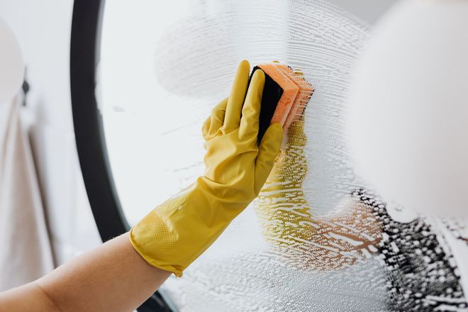 A person wearing yellow gloves is cleaning a window with a sponge.