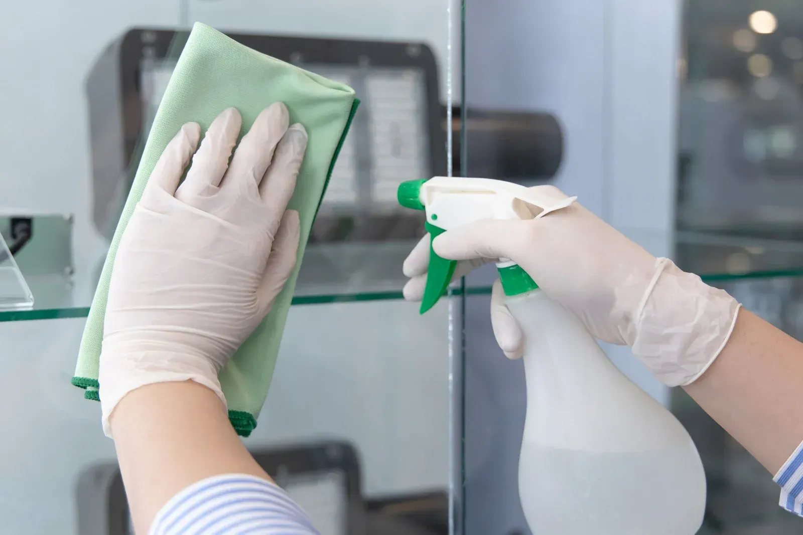 A person is cleaning a glass shelf with a cloth and spray bottle.