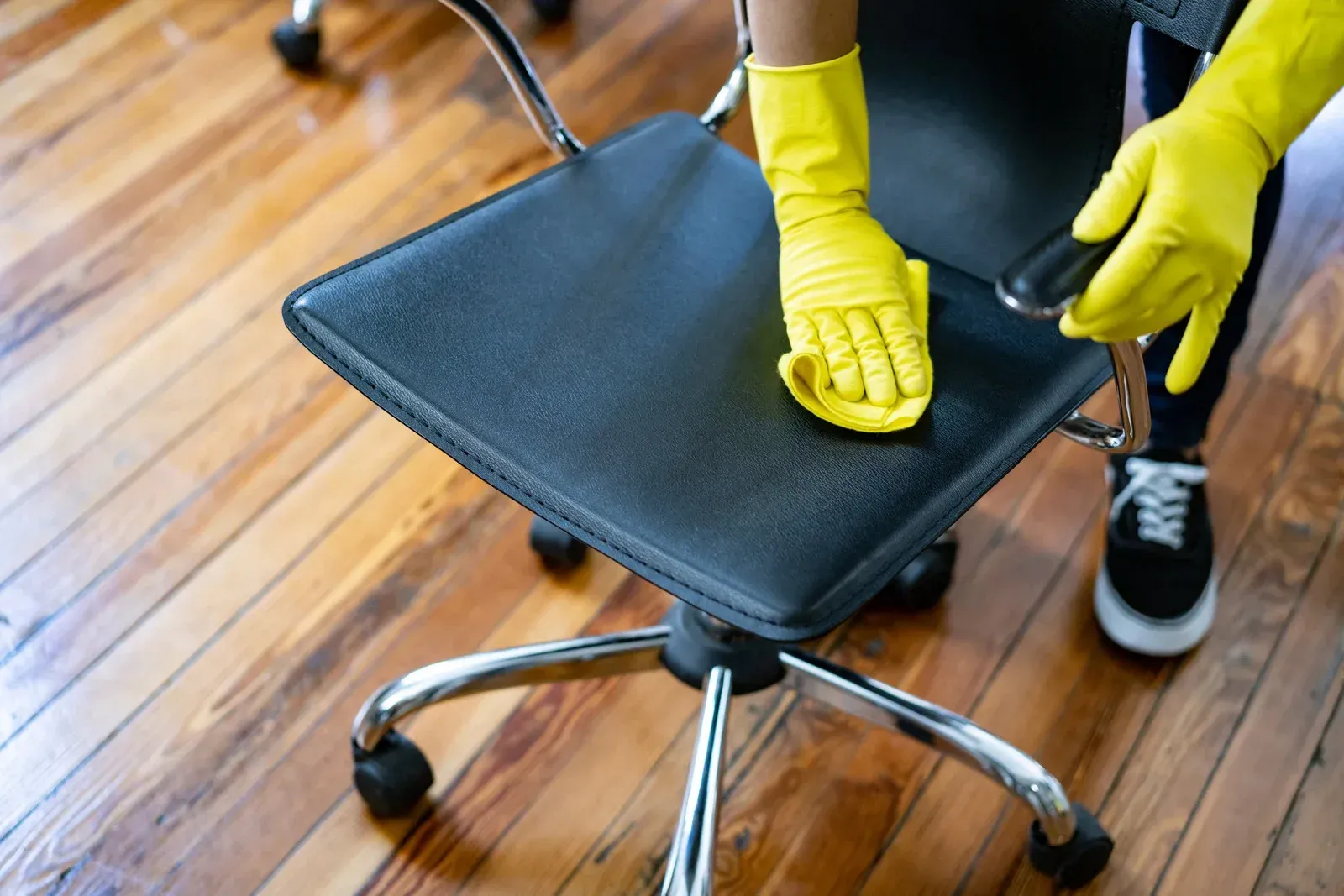 A person wearing yellow gloves is cleaning an office chair.