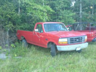 Picture of an old red Ford F150 truck. The truck is sitting in a meadow of grass.
