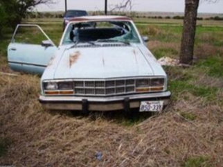 Picture of a old scrap blue junk car. The car is sitting in a yard of grass.
