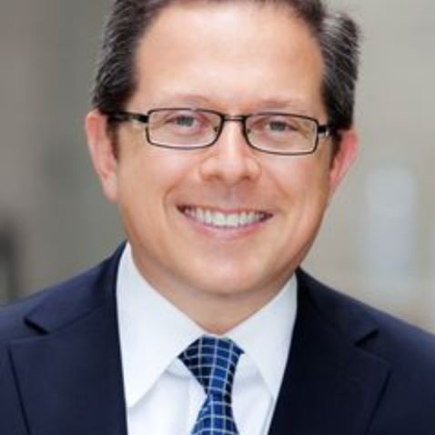A man wearing glasses and a suit and tie is smiling.