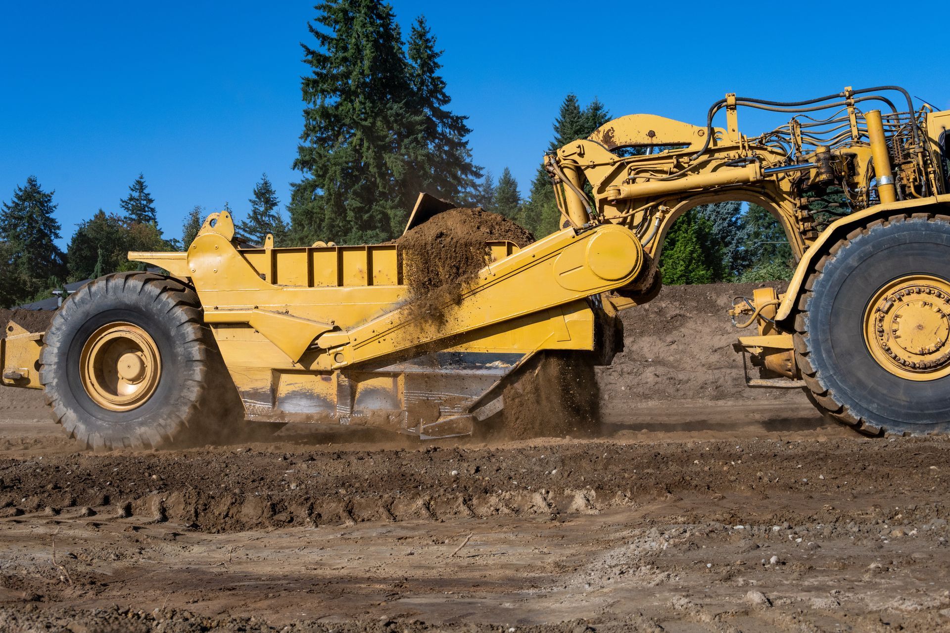 A yellow wheel tractor moves a pile of earth in a construction zone.