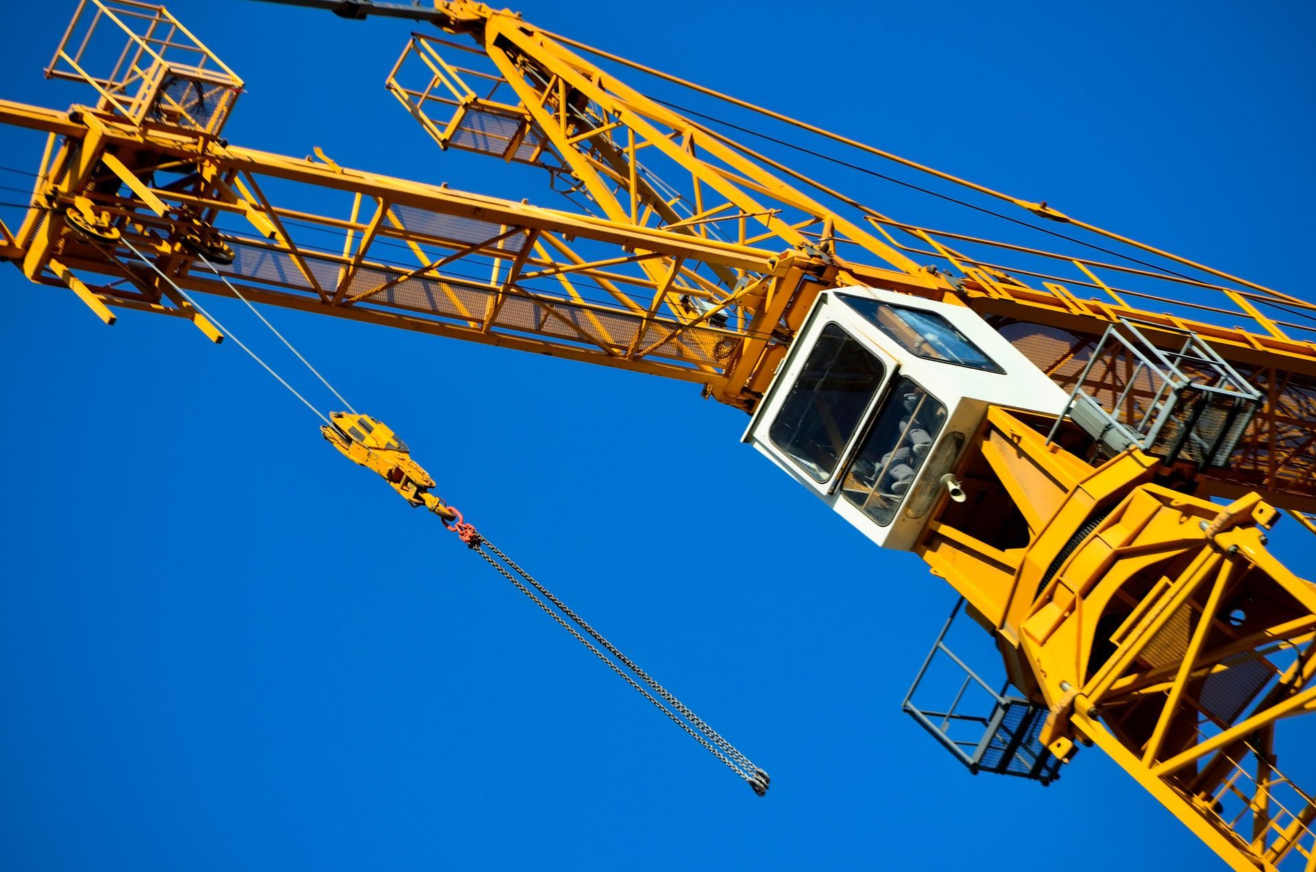 Construction crane lifting equipment against a clear blue sky for hire services.
