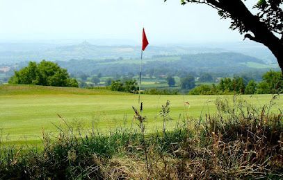 Green golf course with red flag against a distant hilly landscape under a bright sky.