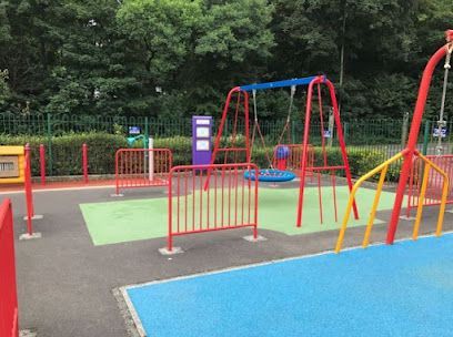 Playground with red and yellow structures, blue and green surfacing, and a swing set.