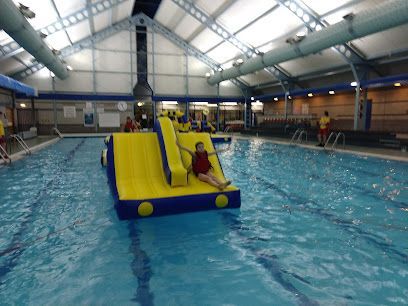 Person sliding down a yellow inflatable slide into a swimming pool; indoor pool setting.