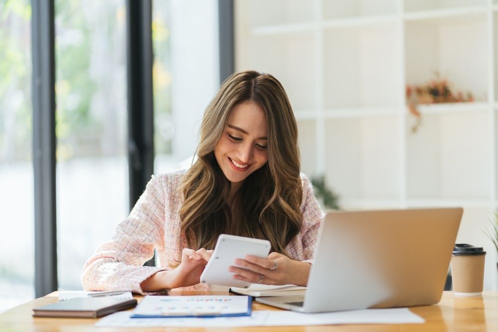 A Woman is Sitting at a Table Using a Calculator with A Laptop and Papers in front of her — Eacham Accounting and Audits in Cairns, QLD