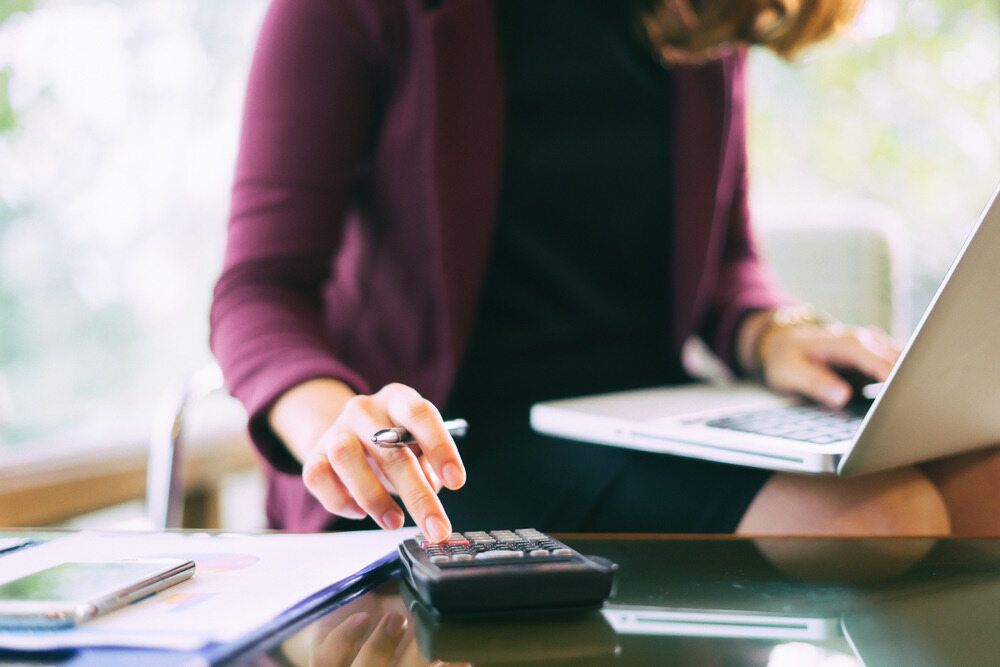 A Woman is Sitting at a Desk Using a Calculator and a Laptop — Eacham Accounting and Audits in Malanda, QLD