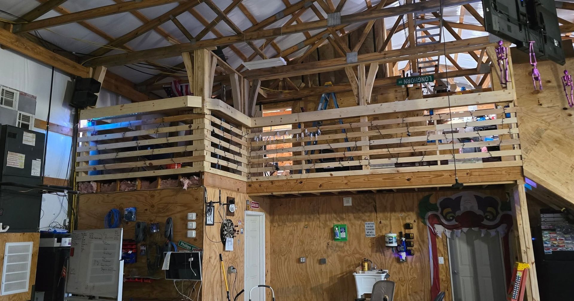 Interior view of a workshop with a wooden mezzanine level, sloped truss ceiling, and plywood walls.