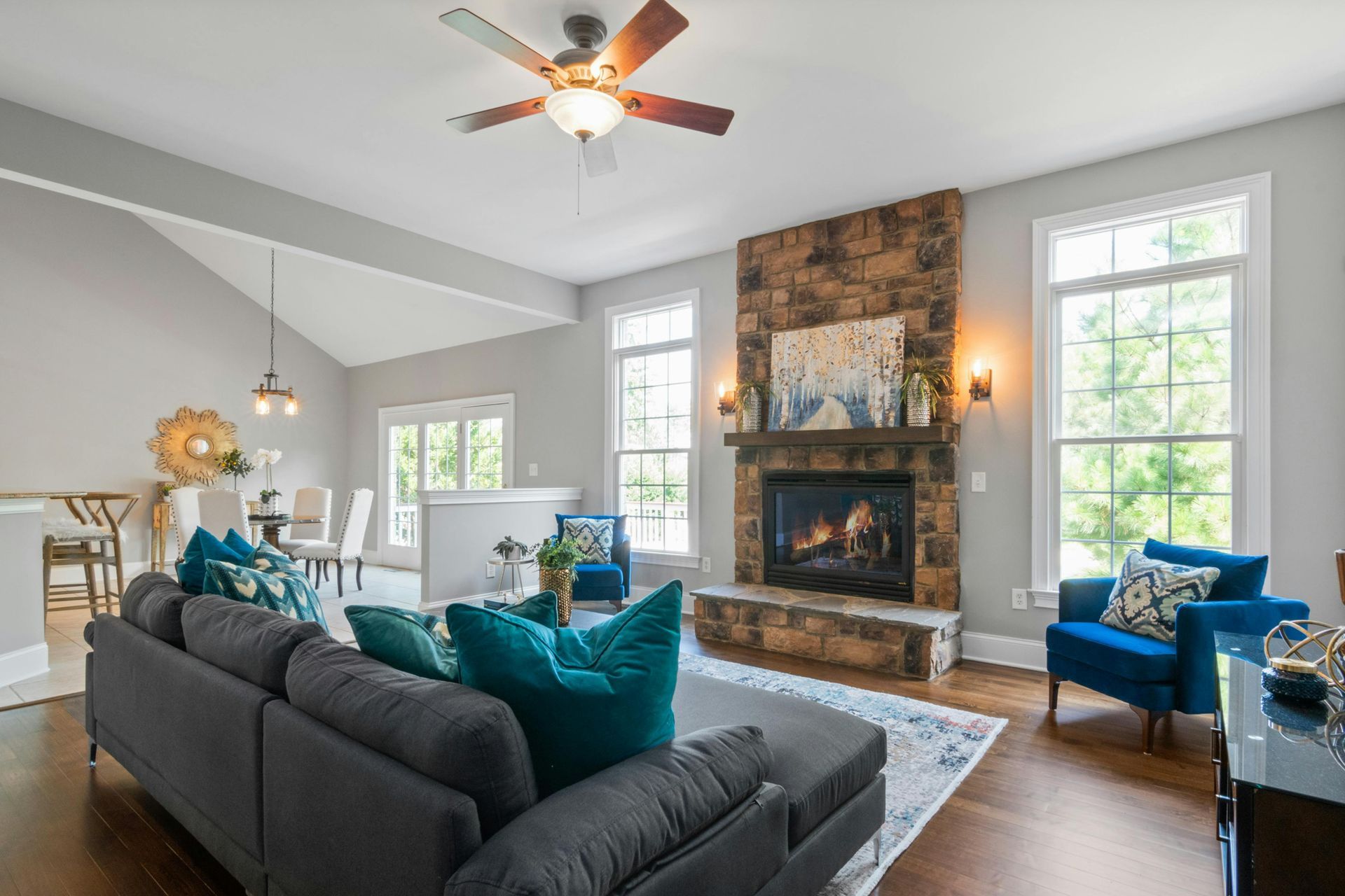 A spacious living room featuring a grey sectional sofa, a stone fireplace, and a dining area in the background.