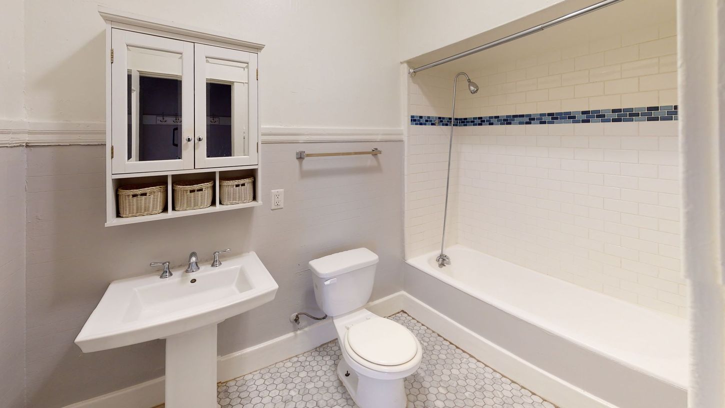 Bathroom with pedestal sink, toilet, and shower/tub. White and gray tile, wall-mounted cabinet.