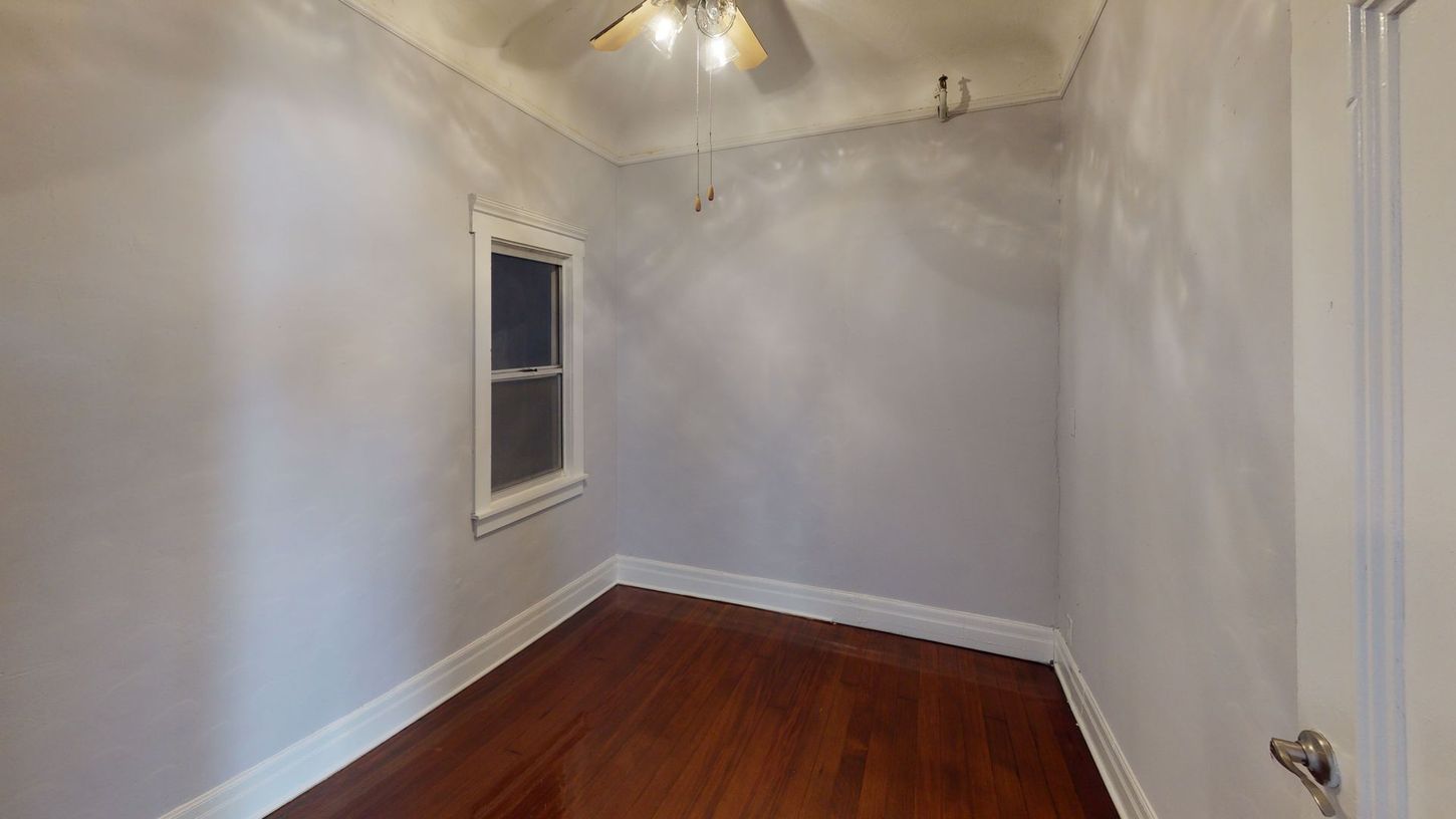 Empty room with a small window, hardwood floors, and gray walls. Ceiling fan and light fixture visible.