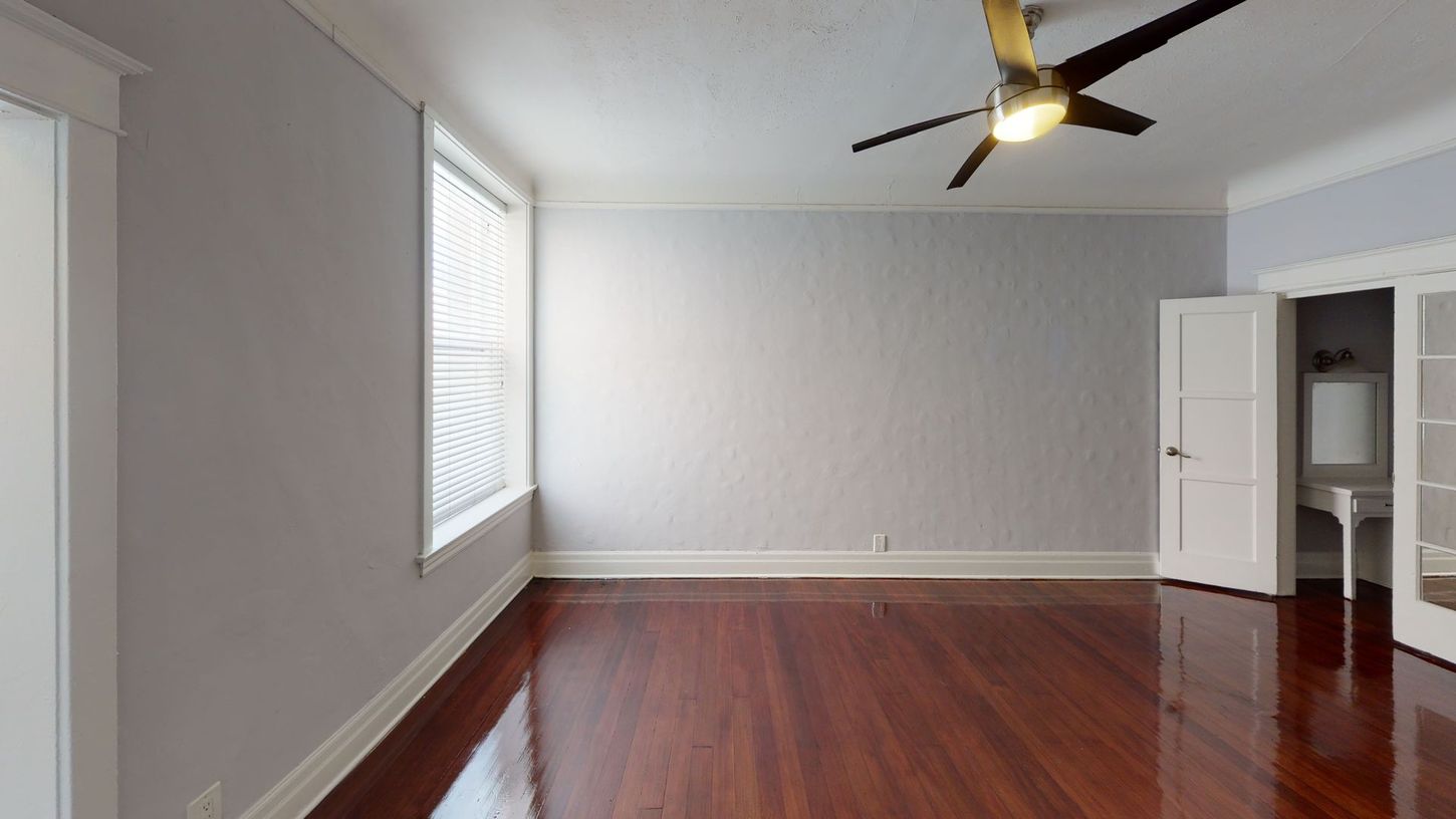 Empty room with hardwood floors, white trim, grey walls, window, and ceiling fan.