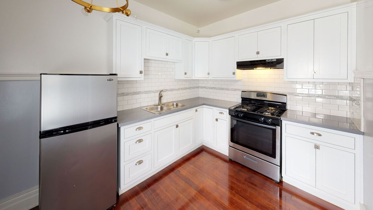 L-shaped kitchen with white cabinets, stainless steel appliances, dark countertops, and hardwood floors.