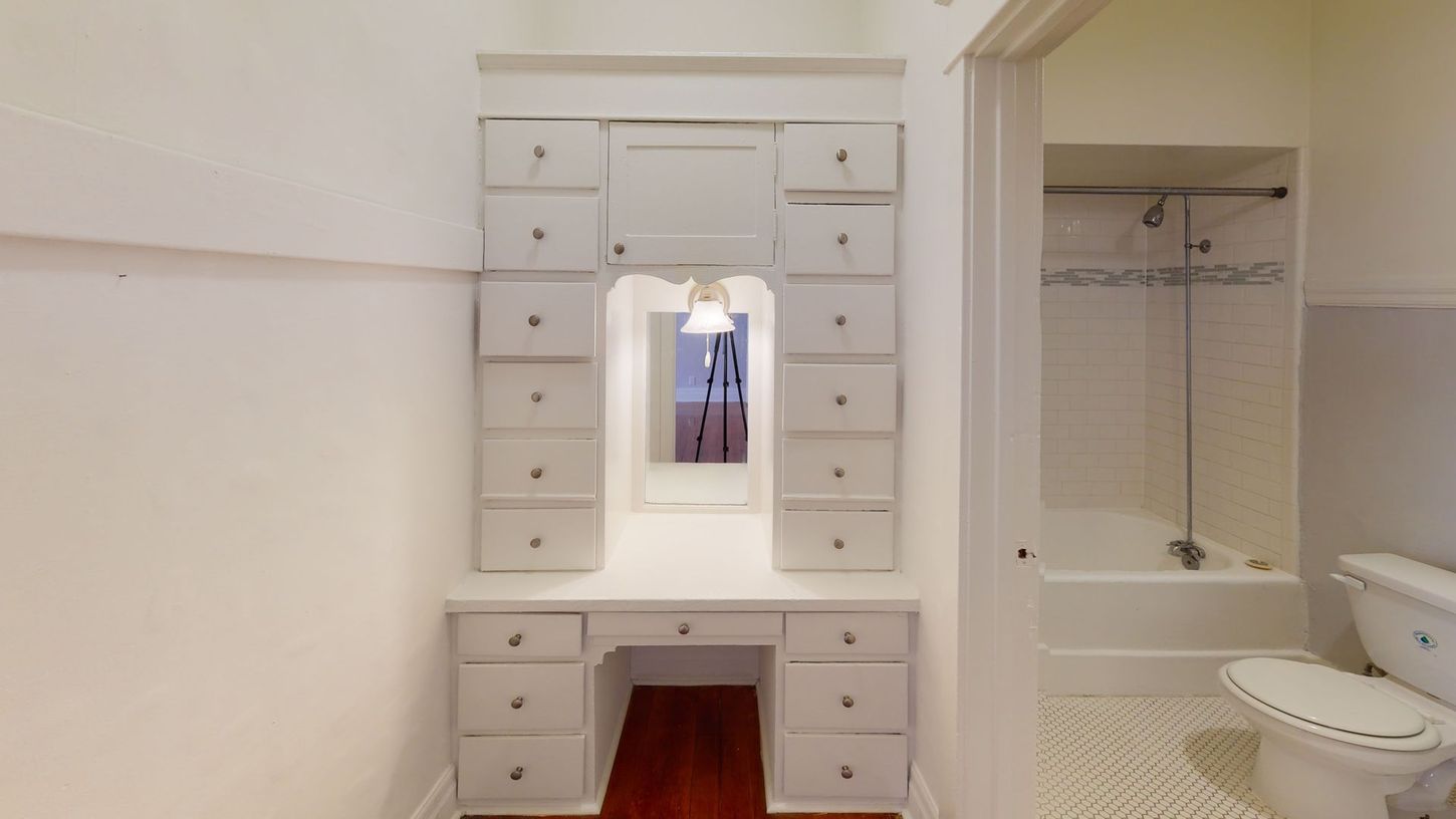 White vanity with mirror and drawers in a bathroom; toilet and bathtub visible.