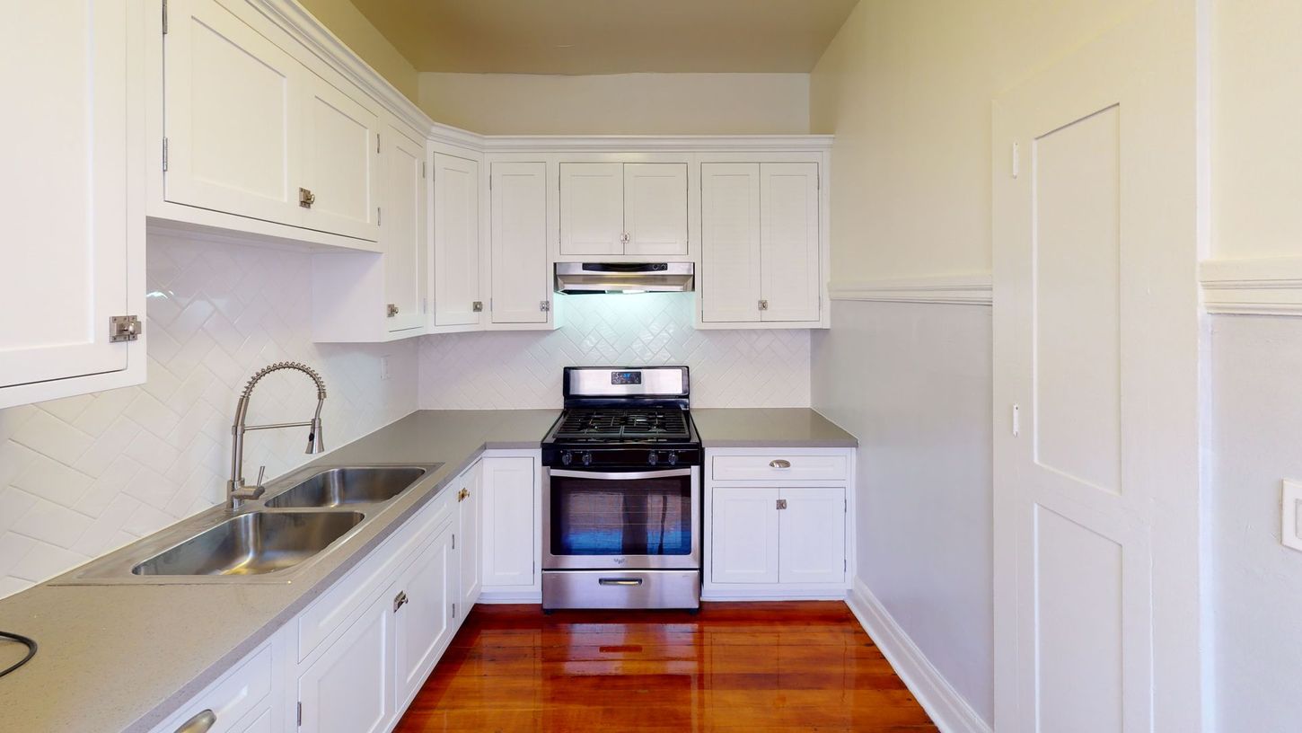 White kitchen with stainless steel appliances and wood flooring.