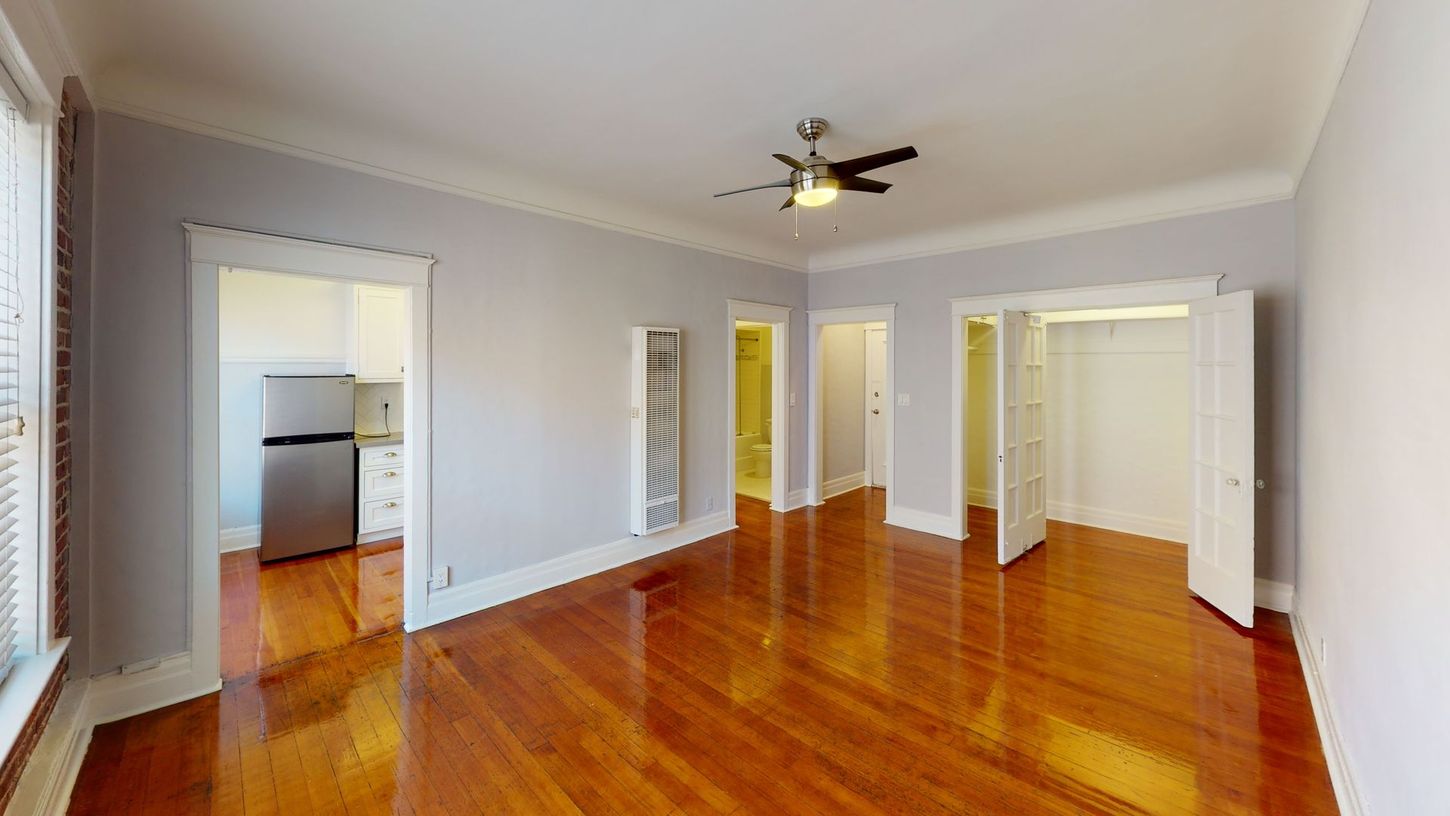 Empty apartment with hardwood floors, doorways, and a ceiling fan.