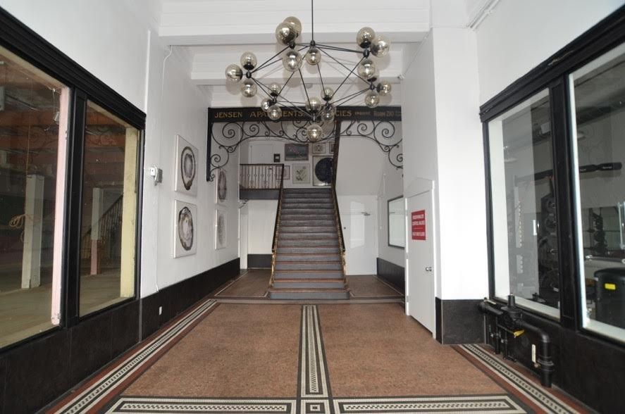 Long hallway with black and white tile floor, stairs, ornate light fixture, and large windows.