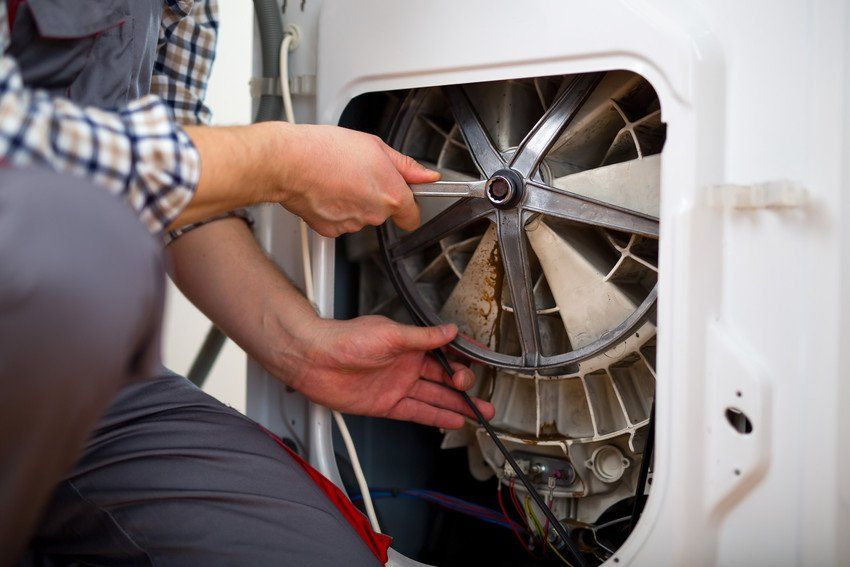A man holding a spanner to the back of a washing machine, which has the back cover off