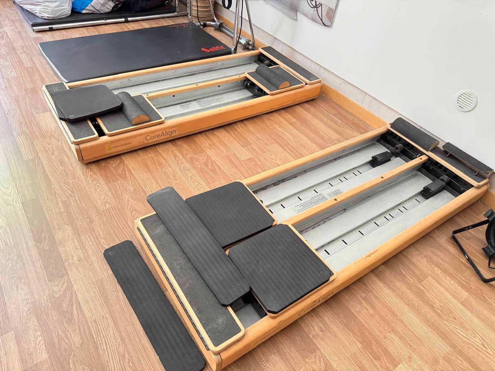 Due reformer Pilates in legno su un pavimento in legno in una stanza.