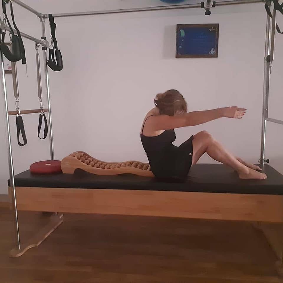 Donna su palla da ginnastica con trainer. Palla blu, pesi viola. L'ambiente è una stanza con pareti e pavimenti chiari.