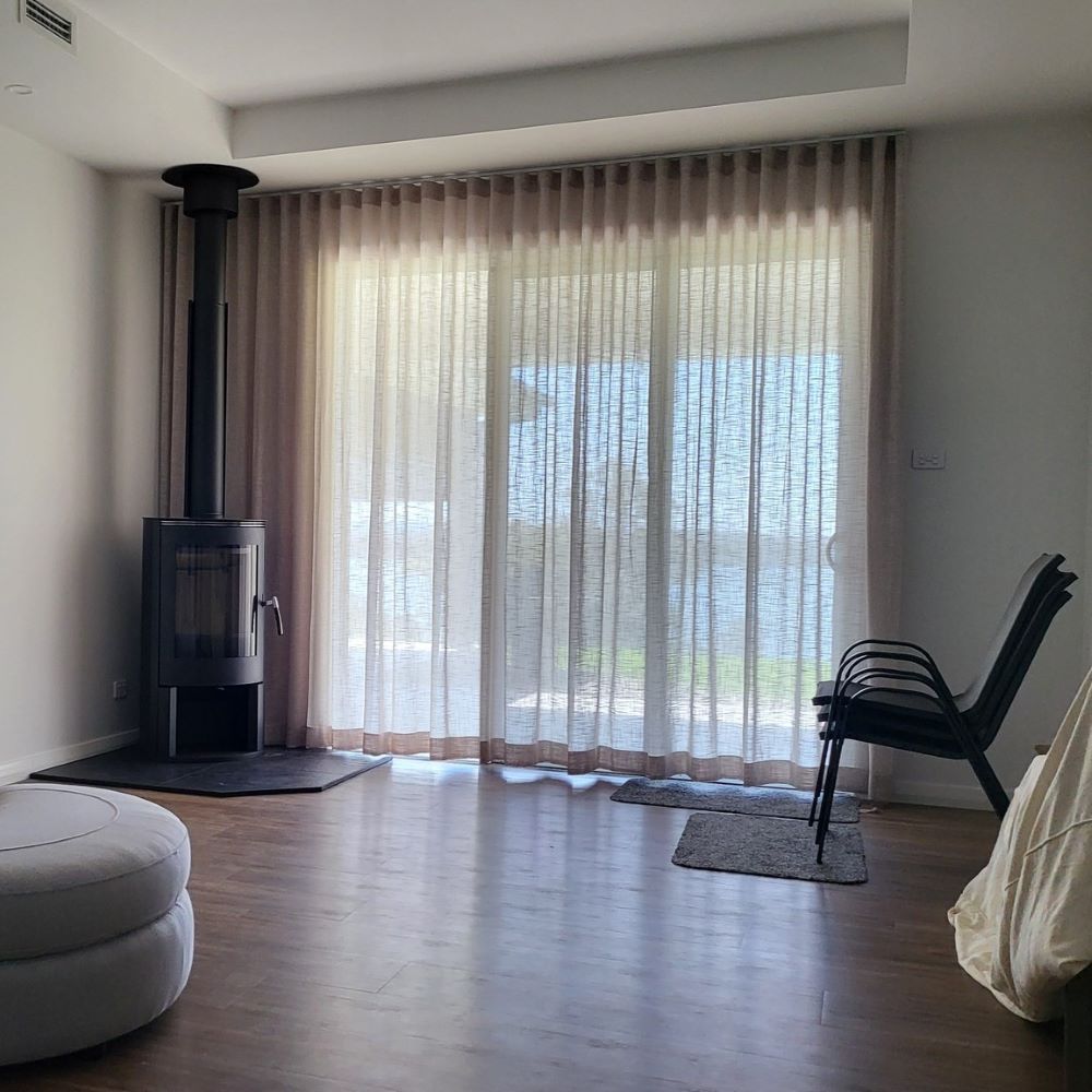 A Living Room With a Fireplace, Chair, Ottoman and Sliding Glass Doors — Elegant Blinds & Awnings in Forster, NSW