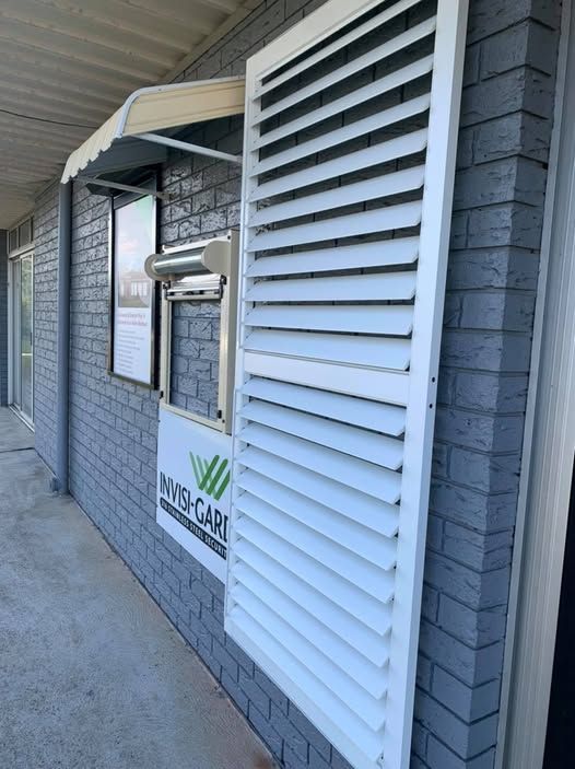 A Brick Building With a White Shutter on the Side of It — Elegant Blinds & Awnings in Forster, NSW