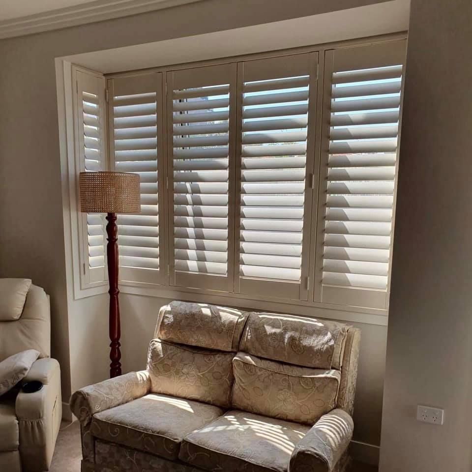 A Living Room With a Couch, Chair, Lamp and Window With Shutters — Elegant Blinds & Awnings in Gloucester, NSW