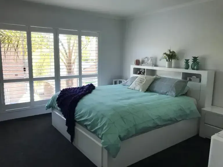 A Bedroom With a Bed and a Window With Shutters — Elegant Blinds & Awnings in Forster, NSW