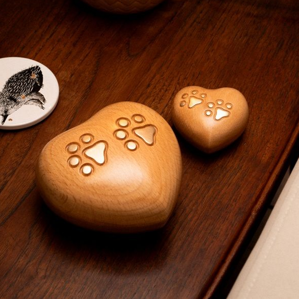 Two wooden heart-shaped urns with paw print cutouts on a dark wooden surface, with a small coaster.